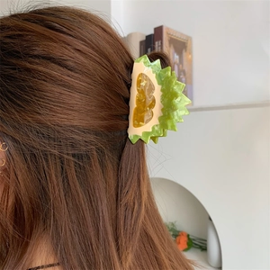 Detail view of a creative durian-shaped acetate hair claw clip worn on long brown hair