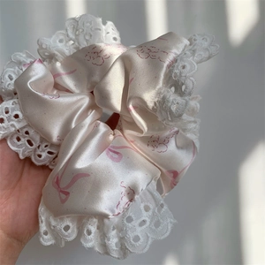 Detailed close-up of glossy satin scrunchie with pink bow patterns and white lace edges