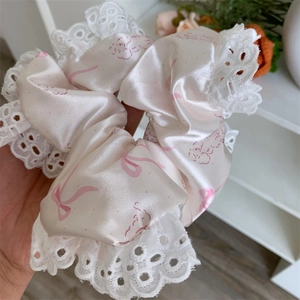 Close-up of pink satin hair scrunchie with white lace trim and bow pattern texture