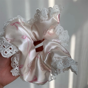 Detail view of pink satin scrunchie with lace trim and bow patterns held in hand