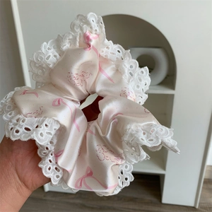 Close-up of beige silk scrunchie with pink bow patterns and white lace floral borders
