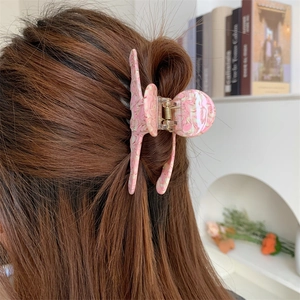 Rear view of a pink marble texture acetate shark clip holding long brown hair in a cozy room