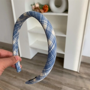 Close-up of a slim blue and white checkered headband held in a home setting