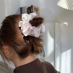 Pink silk bow scrunchie with cute patterns worn on a model in a cozy indoor setting