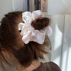 Close-up of a premium pearly white satin hair scrunchie with pink floral patterns