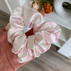 Close-up of pink satin hair scrunchie with bow prints and elegant ruffled lace edges