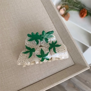 Detailed top view of a cream strawberry claw clip with green leaves on a textured tray