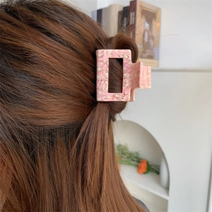 Pink marble texture acetate hair claw clip styled on long brown hair in minimalist room