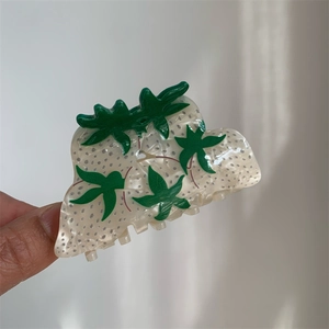 Detailed view of an acetate strawberry hair claw clip with pearl finish and green leaf accents