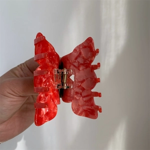 Close-up of a red butterfly hair claw with stone texture finish and metal spring