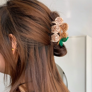 Medium lotus seed pod hair claw clip in beige acetate with green leaf accent on brown hair