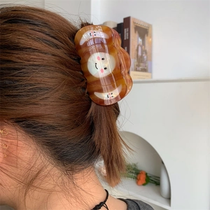 Detail showing acetate hair claw clip with smiley face pattern holding a brunette ponytail