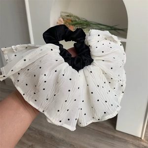 Close-up of a large pleated scrunchie featuring classic black and white polka dot pattern