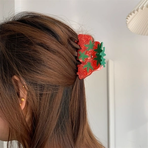 Detail of a medium red strawberry claw clip with realistic seeds on a woman's hair