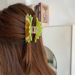 Action shot of a green and yellow durian-shaped acetate claw clip on brown long hair