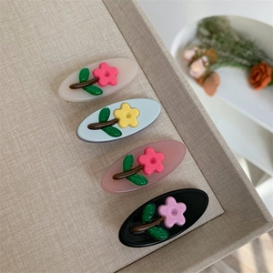 Dettaglio di quattro fermagli per capelli in acetato con fiori in beige, blu e rosa