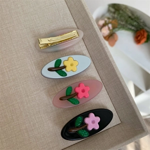 Dettaglio di quattro fermagli in acetato con fiori 3D su un vassoio in tessuto beige