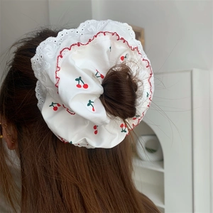 Dettaglio di scrunchie in pizzo bianco con ciliegie indossato su uno chignon