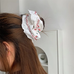 Dettaglio dell'elastico per capelli bianco con stampa ciliegia e pizzo su uno chignon