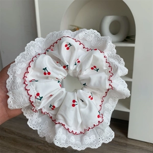 Dettaglio di scrunchie in pizzo bianco con motivo ciliegia e bordi ondulati rossi