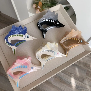 Detailed view of fish-shaped acetate hair claws in blue, black, pink, beige, and brown