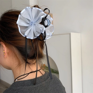 Dettaglio di un fermaglio per capelli con fiori in rete blu e nastri neri indossato dietro