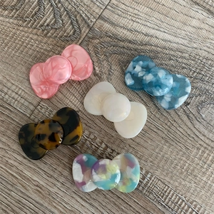 Detail showing five-piece candy-colored acetate bow hair clips with marble texture on wood