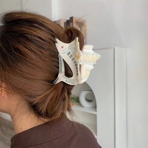 Detail of sailfish-shaped acetate hair claw clip holding hair in a high-quality styling view