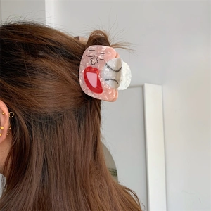 Detailed view of an acetate shark hair claw with artistic face design on brown hair