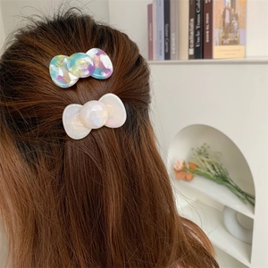 Pastel acetate hair clips including a white bow and tricolor disc on brown hair