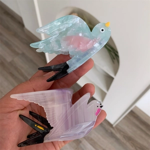 Detailaufnahme von vogelförmigen Haarklammern aus Acetat in Pastellblau und Lila