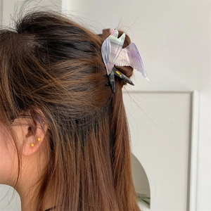 Detail einer vogelförmigen Acetat-Haarklammer in Lila und Weiß auf braunem Haar