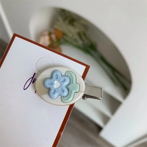Dettaglio di un fermaglio per capelli ovale crema con rilievo floreale blu su scheda
