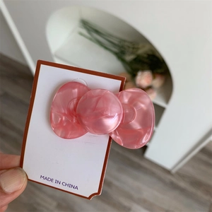 Detailed view of a pink acetate bow hair clip with marbled texture on a display card