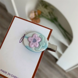 Dettaglio del fermaglio per capelli in acetato con fiore rosa su base ovale blu