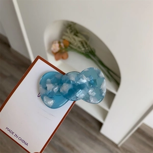 Macro detail of blue acetate bow hair clip with white cloud texture on display card