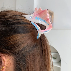 Detail of pink marble acetate hair claw clip in marlin fish shape on long hair