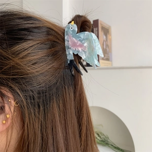 Nahaufnahme der vogelförmigen Haarklammer aus Acetat mit blau-rosa Farbverlauf im Haar