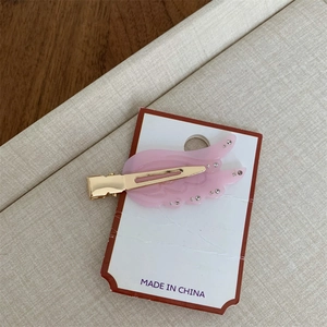 Detaillierte Nahaufnahme einer rosa flügelförmigen Acetat-Haarspange mit Strass