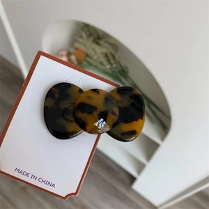 Detail showing high-gloss acetate hair clip with tortoiseshell texture and rounded bow design
