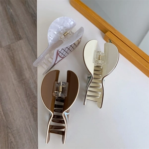 Detailed close-up of three acetate tennis-style hair claws in white, beige and brown tones
