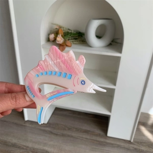 Detailed view of fish-shaped acetate hair claw clip with pink marble texture in hand