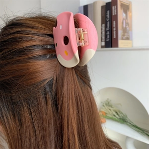 Pink donut hair claw clip shown on long brown hair in a natural lifestyle setting