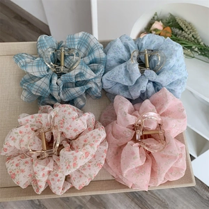 Detail of four floral fabric hair claws in blue and pink chiffon on a beige linen tray