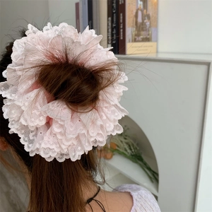 Macro shot of layered pink lace scrunchie with intricate wavy edges on a messy bun