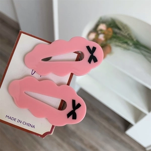Gros plan de barrettes à cheveux en résine rose ondulée avec motif nœud noir