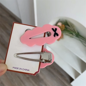 Détail de deux pinces à cheveux roses en acrylique avec motifs nœuds sur emballage
