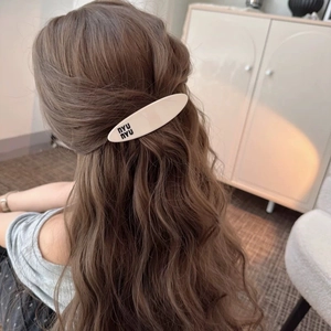 Minimalist cream white oval hair clip with black nyu nyu lettering on brown wavy hair