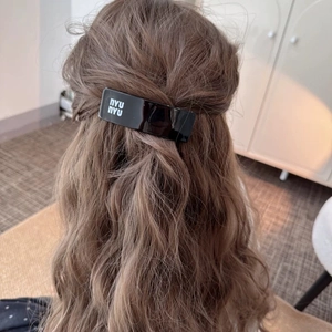 Detail view of a black acrylic hair clip with nyu nyu text on long wavy brown hair