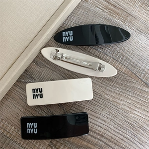 Detail view of NYU NYU letter hair clips in black and cream white on a wood background